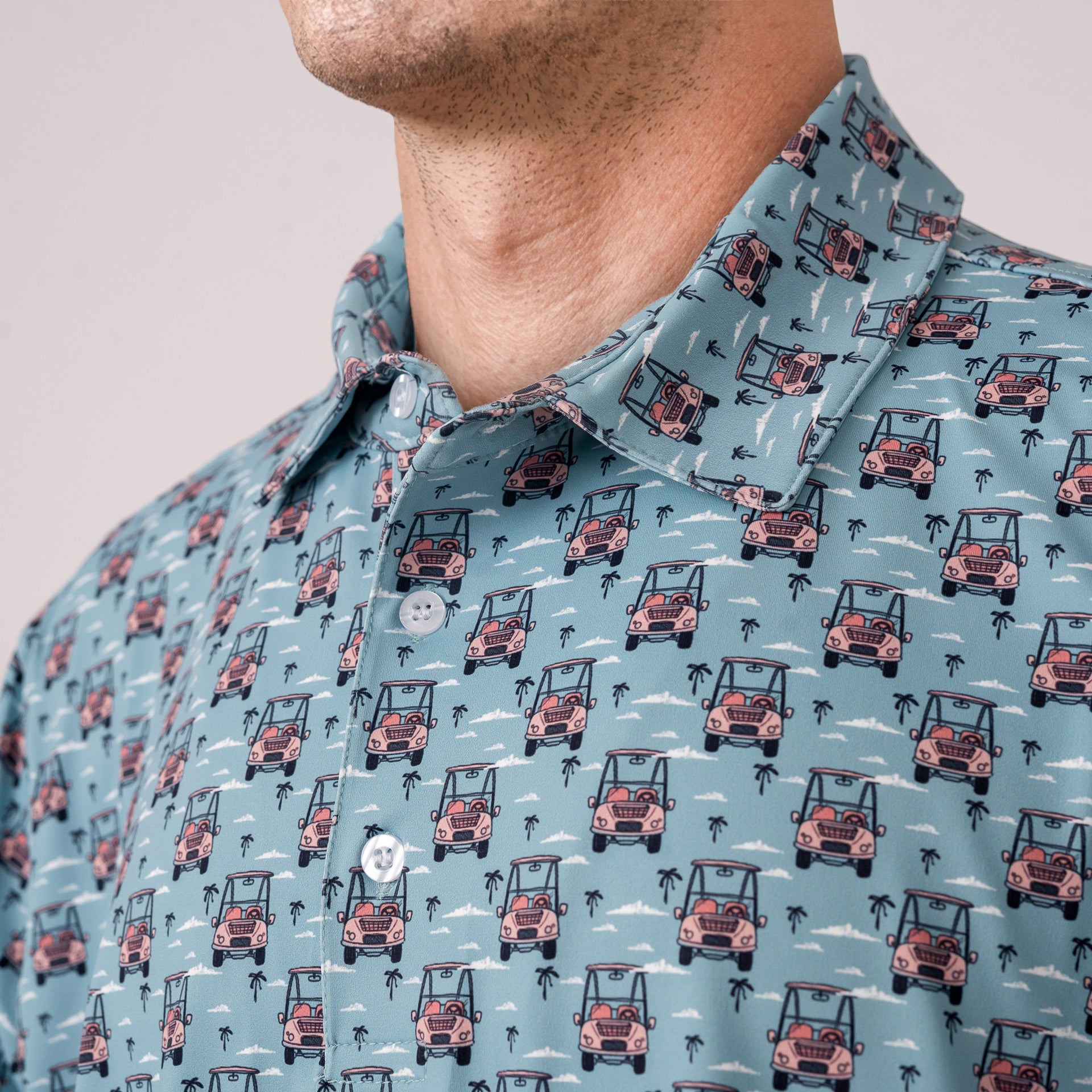Close-up of a person wearing a dusty blue shirt with a pink golf cart pattern