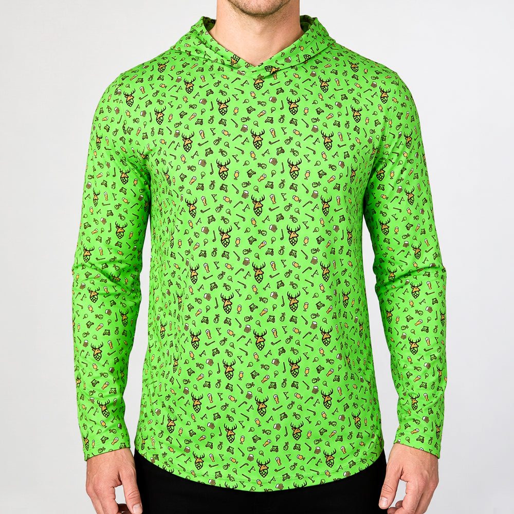 A man wearing a bright green long-sleeve hooded shirt with an all-over repeating pattern of small illustrated characters, photographed against a plain light gray studio background.