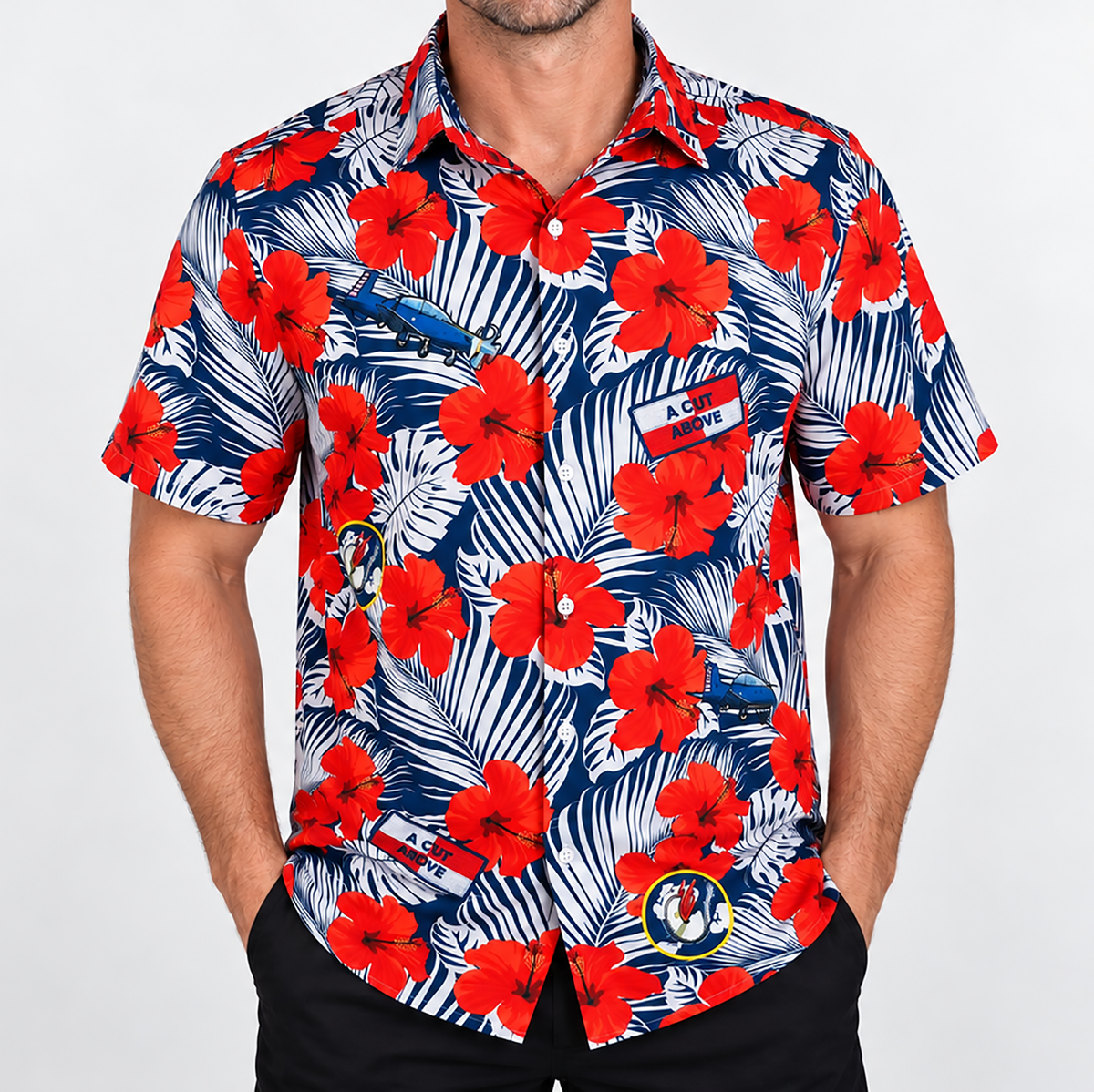 A man wearing a short-sleeve button-down shirt with a white, red, and blue tropical floral and monstera leaf print, featuring custom logos.