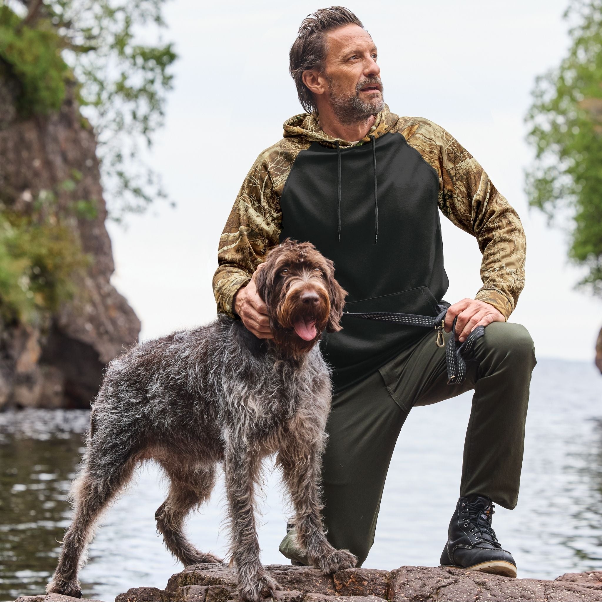 Man and dog by a body of water wearing Realtree Edge camouflage and black clothing.