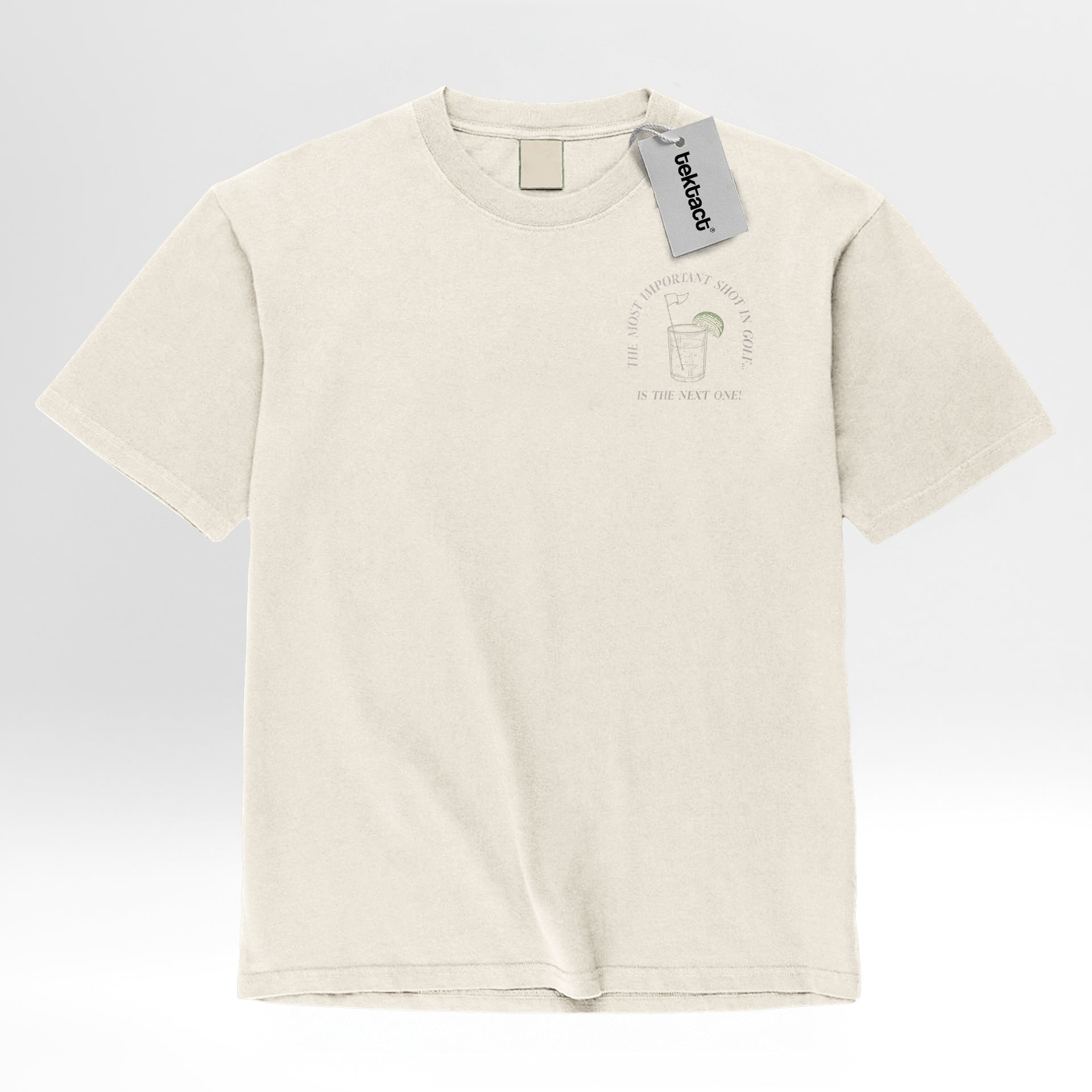 Beige t-shirt with a graphic design and text on the left chest 'The Most Important Shot In Golf Is The Next One'.